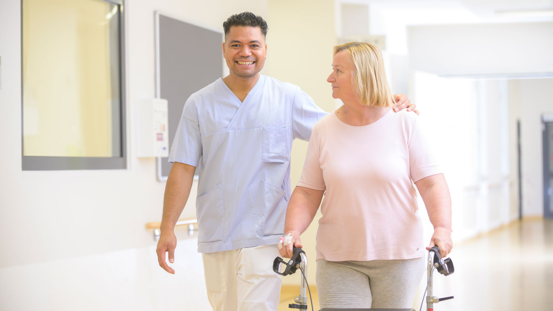 Ein Pfleger geht mit einer Patientin über einen Krankenhausflur