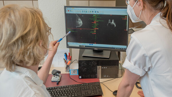 Zwei Ärztinnen betrachten einen Bildschirm, auf dem eine Röntgenaufnahme einer Brust zu sehen ist. 