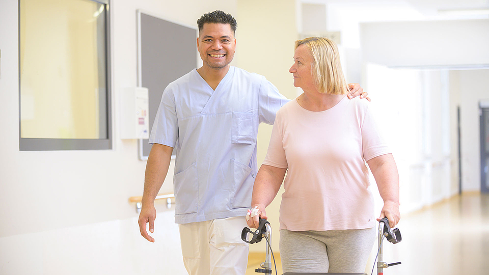 Ein Pfleger geht mit einer Patientin über einen Krankenhausflur