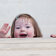Ein Mädchen mit Downsyndrom winkt und lacht