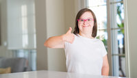 Down syndrome woman at home happy with big smile doing ok sign, thumb up with fingers, excellent sign
