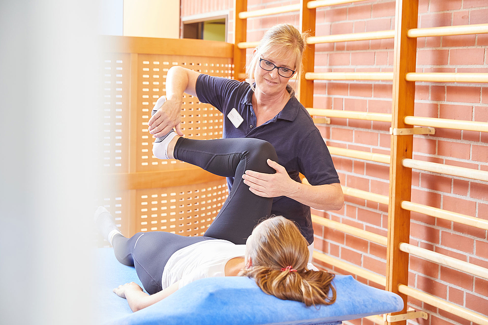 Eine Physiotherapeutin behandelt eine Patientin, die auf einer Liege liegt.